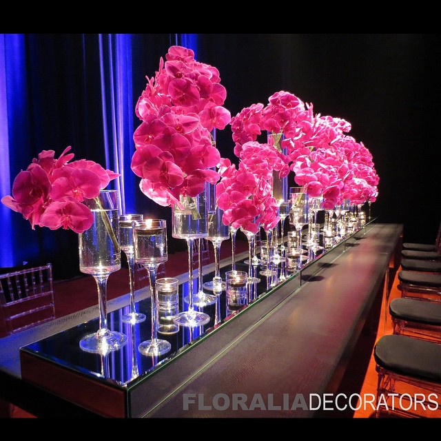 Tall stemmed candle holder vases with fuchsia orchids on long rectangle table
